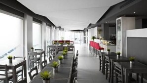 Un espace de restauration moderne, doté de longues tables et de chaises, de grandes fenêtres et d’un bar.