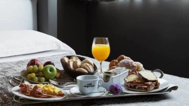 Un plateau de petit-déjeuner avec des croissants, un sandwich, des fruits et un verre de jus d’orange, posé sur une table dans une chambre d’hôtel.