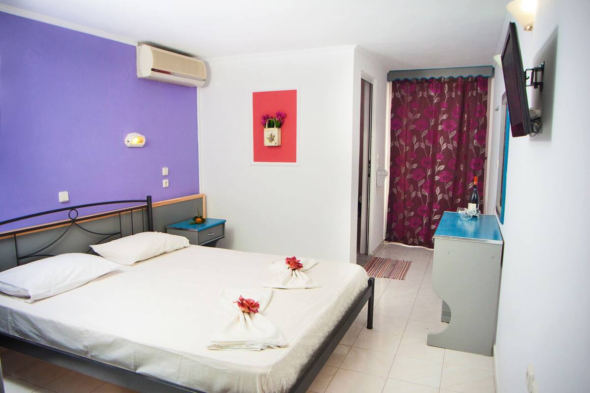 Habitación de hotel con cama, mesita de noche, escritorio y baño visible a través de una puerta abierta.