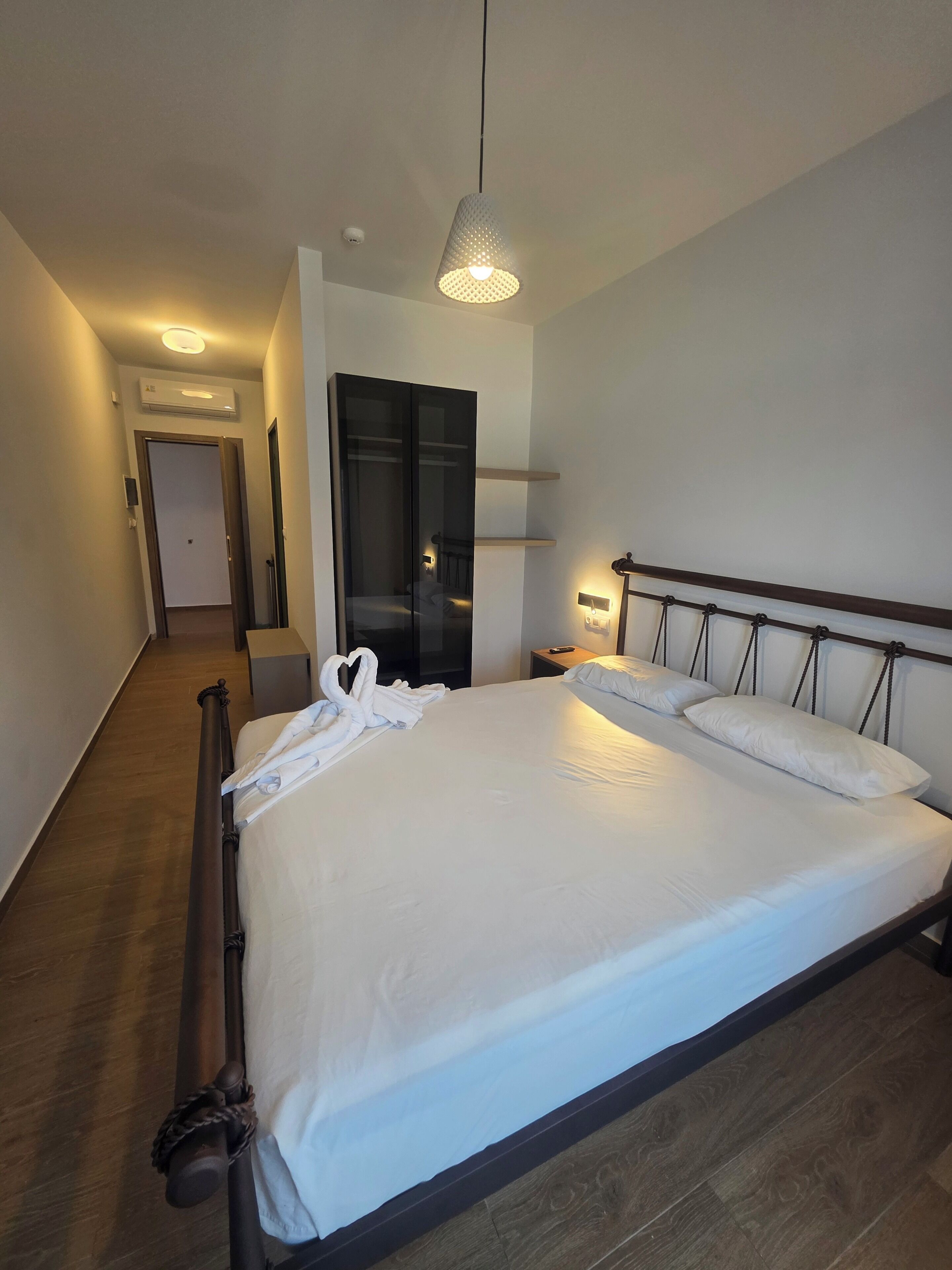 Moderni hotellihuone, jossa on suuri sänky, yöpöytä, lamppu ja vaatekaappi.