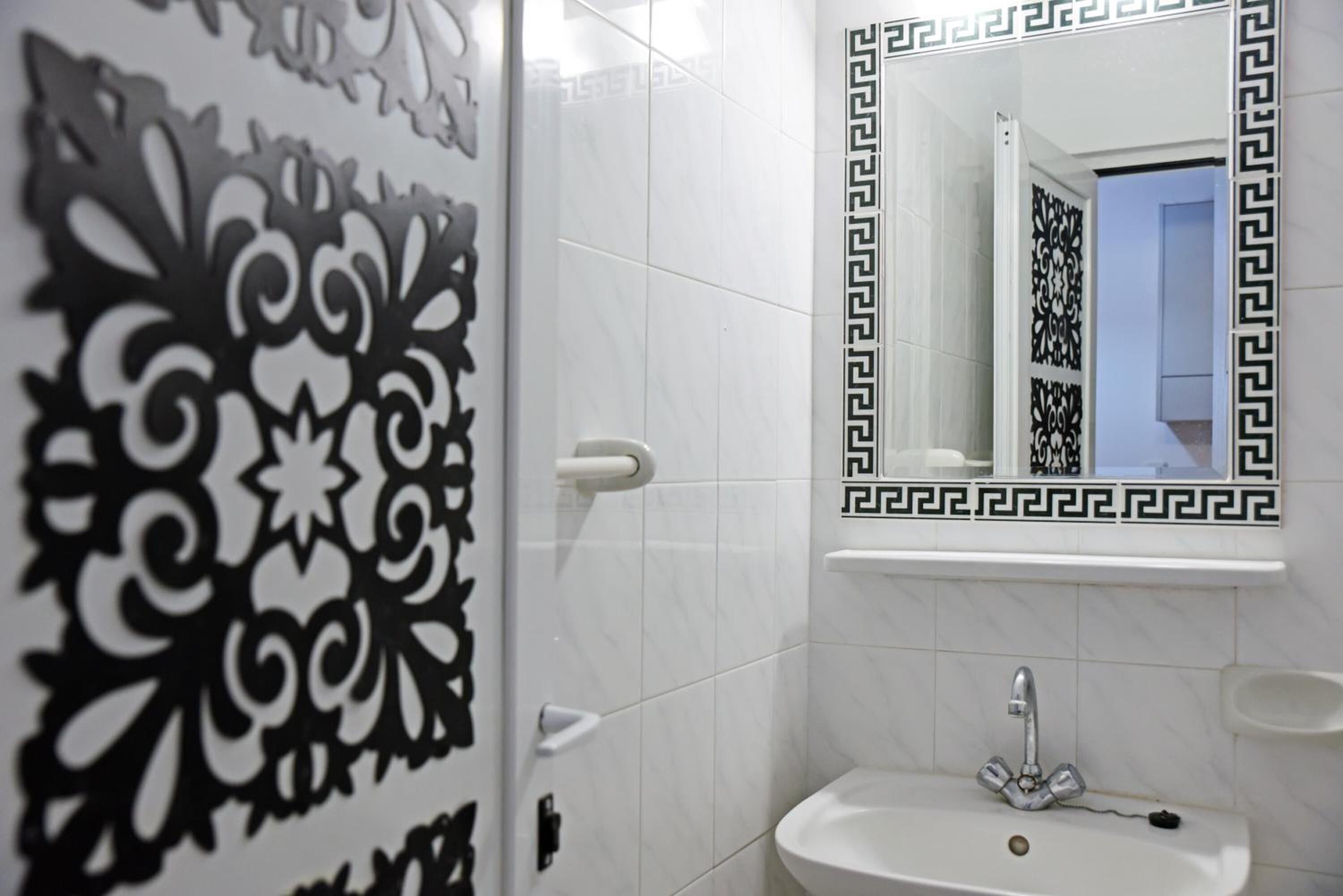 Un baño con lavamanos blanco, un espejo con marco negro y motivos decorativos en la pared.