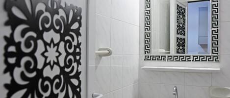 Un baño con lavamanos blanco, un espejo con marco negro y motivos decorativos en la pared.