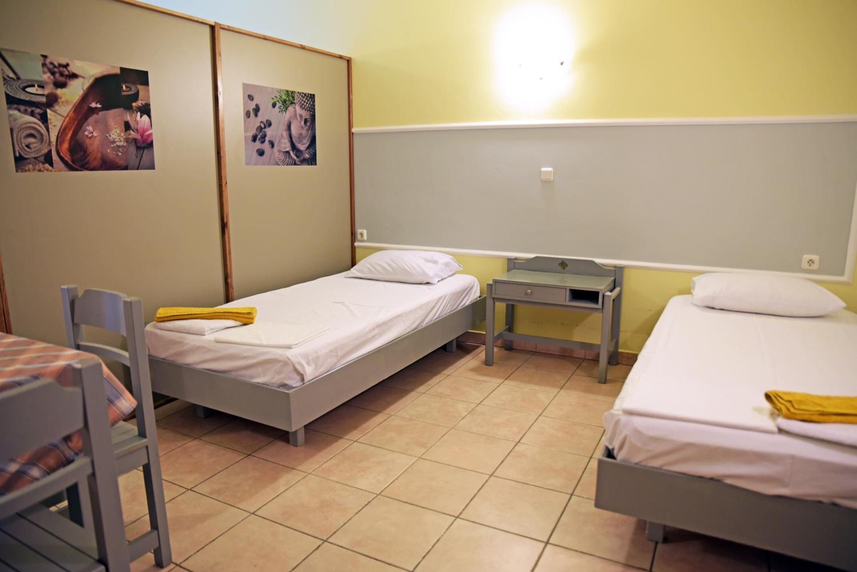 A dormitory room with two single beds, a small table, and a chair.