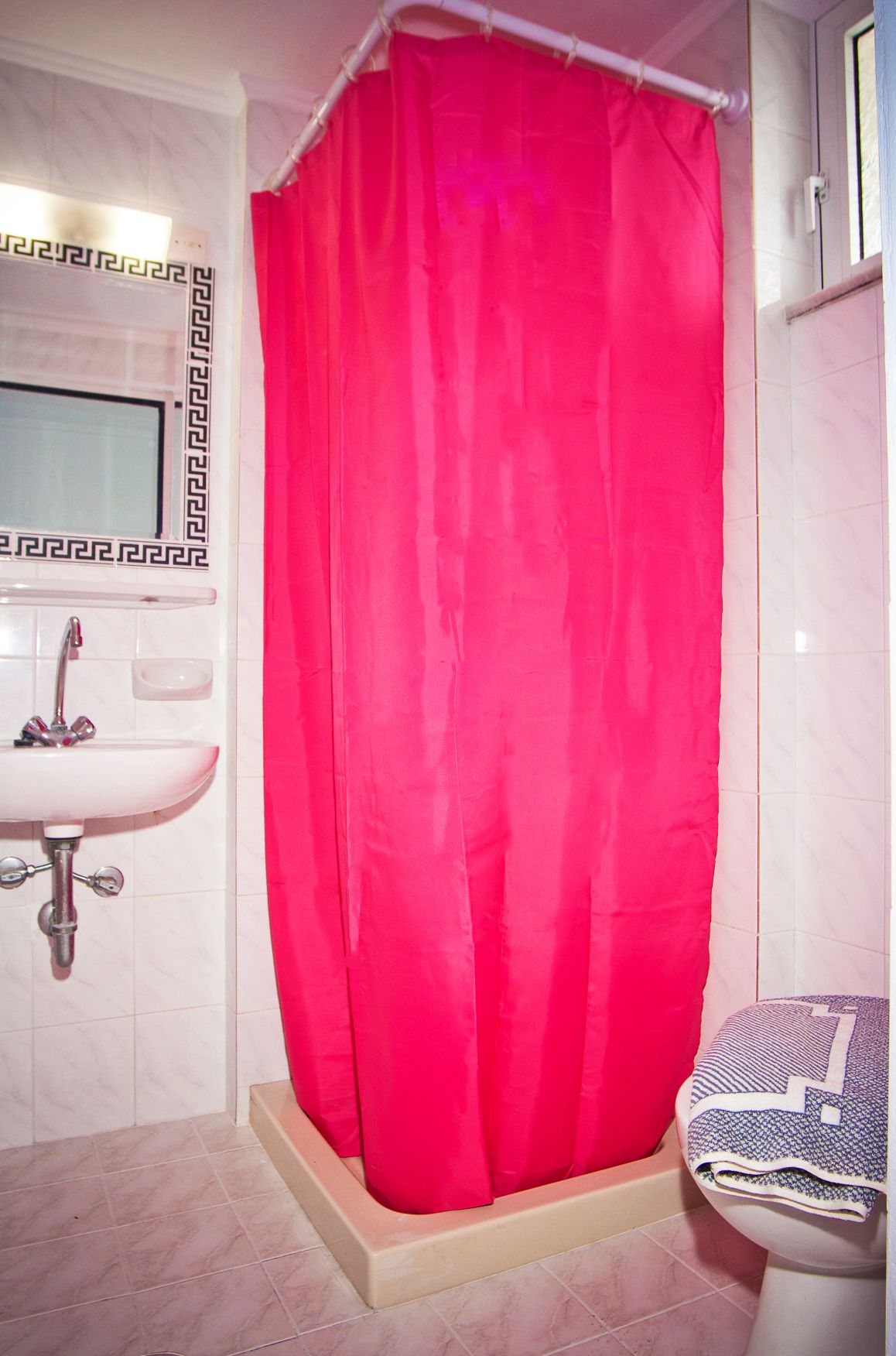 A bathroom with a white sink, a mirror with a black and white frame, and a red shower curtain.