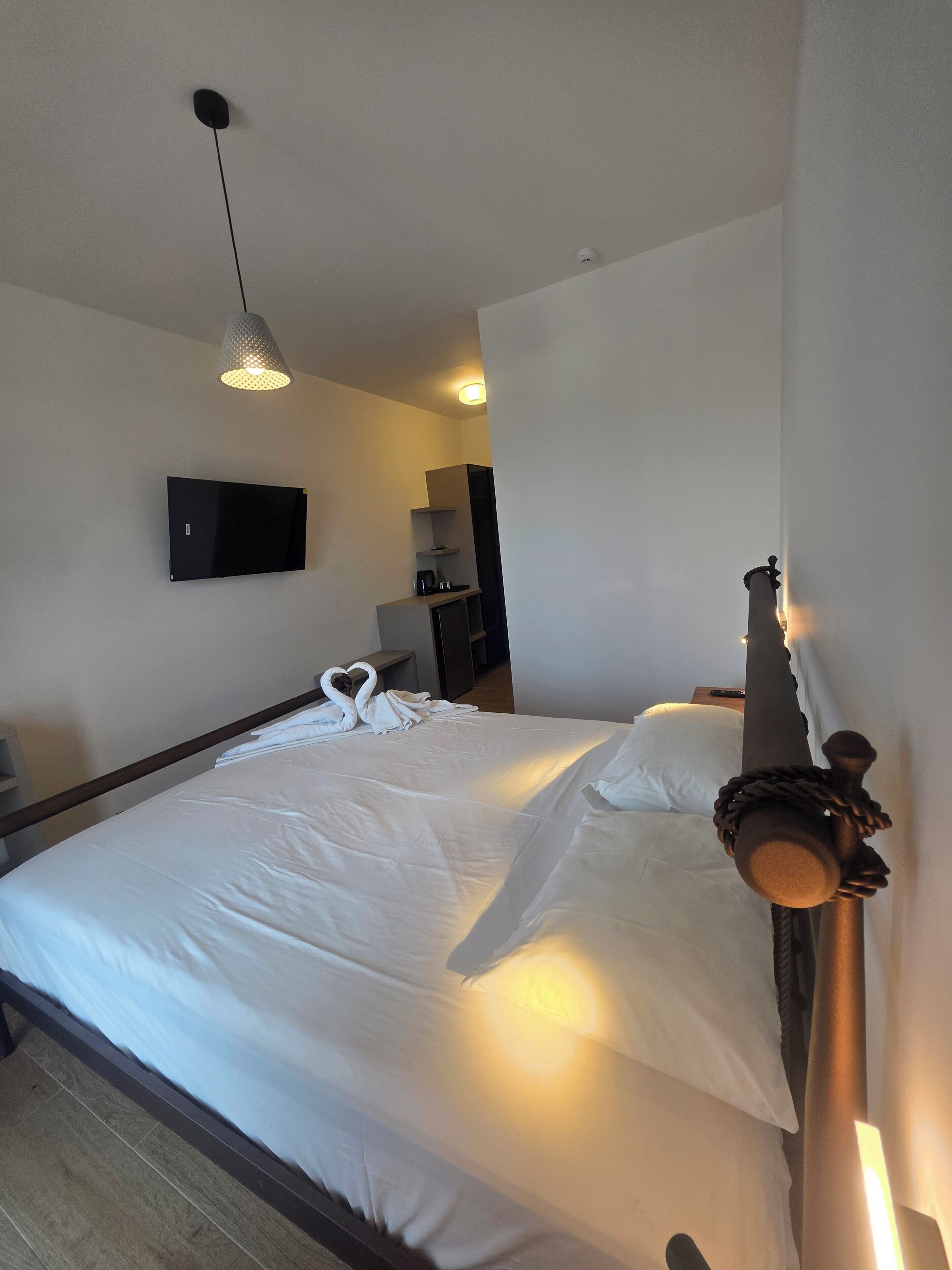 Una habitación de hotel con una cama, un televisor montado en la pared, una lámpara colgante y un cabecero de madera.