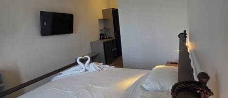 Una habitación de hotel con una cama, un televisor montado en la pared, una lámpara colgante y un cabecero de madera.