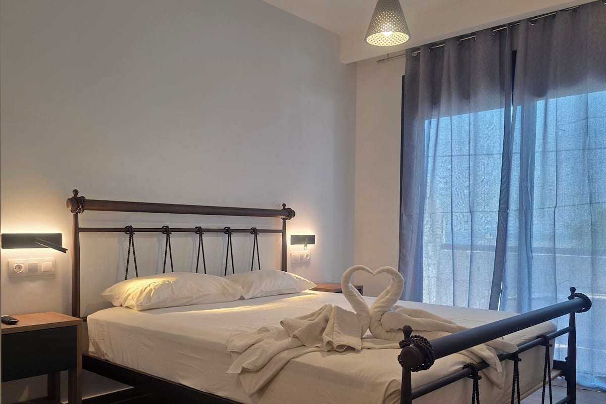 Un dormitorio moderno con estructura de cama de madera, una mesita de noche, una lámpara y una ventana con cortinas.