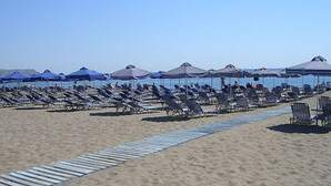 A beach with rows of sun loungers and umbrellas, a clear sky, and a calm sea in the background. - Falirala Central (Rhodes)