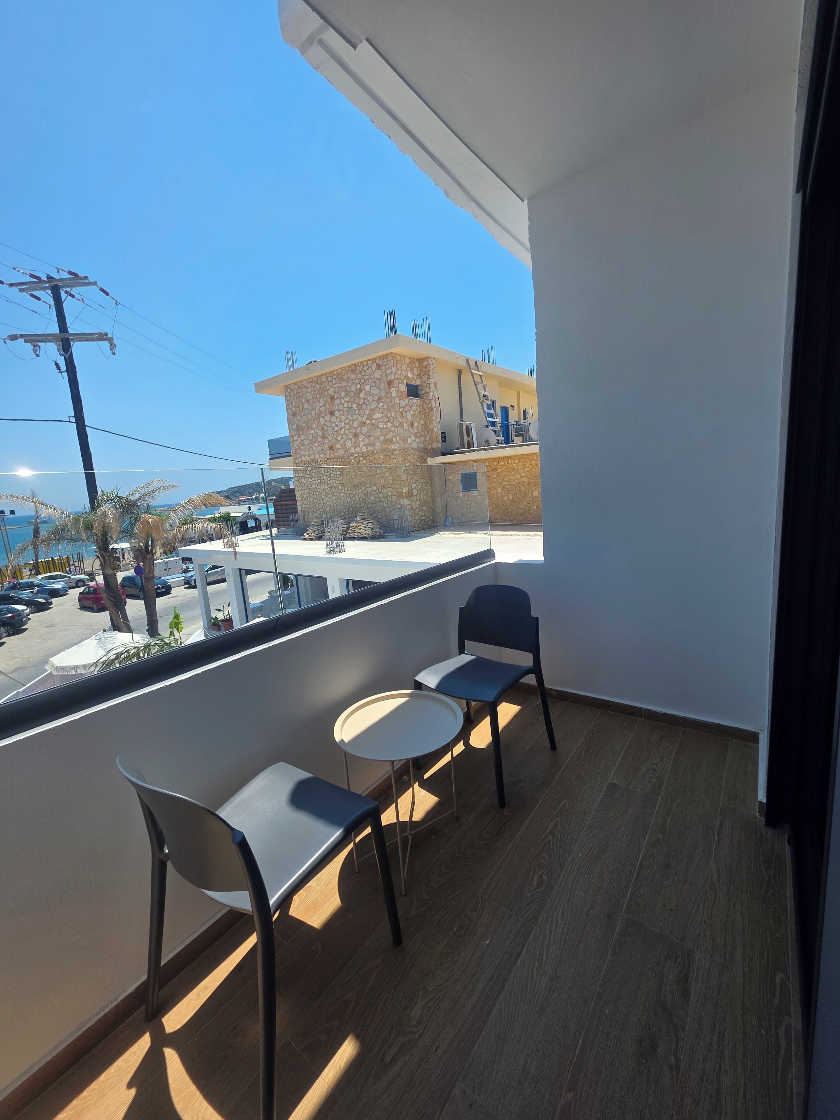 A balcony with a table and chairs, a view of a building under construction, and a clear sky.