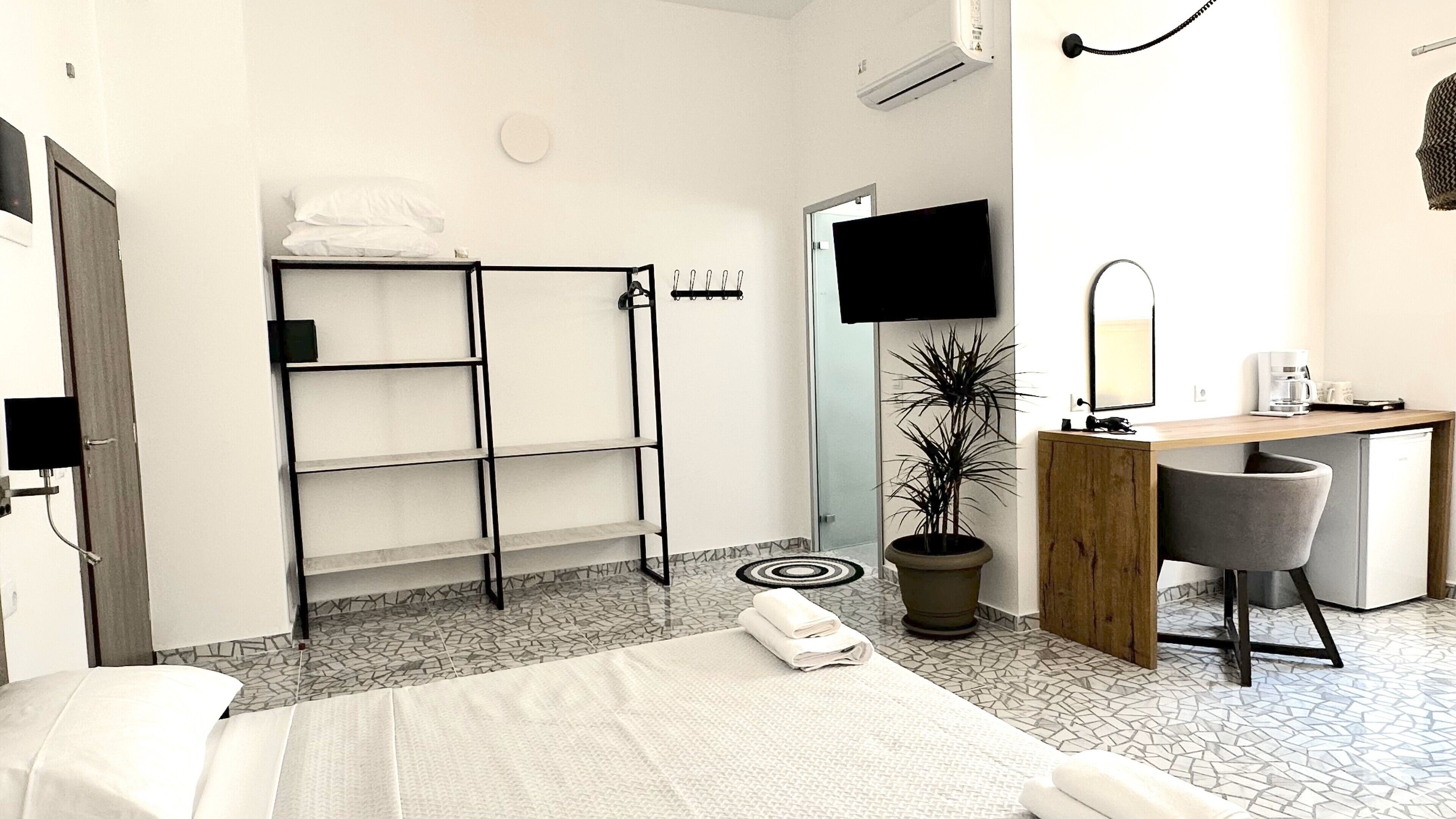 A hotel room with a bed, a desk, a chair, a potted plant, and a TV.