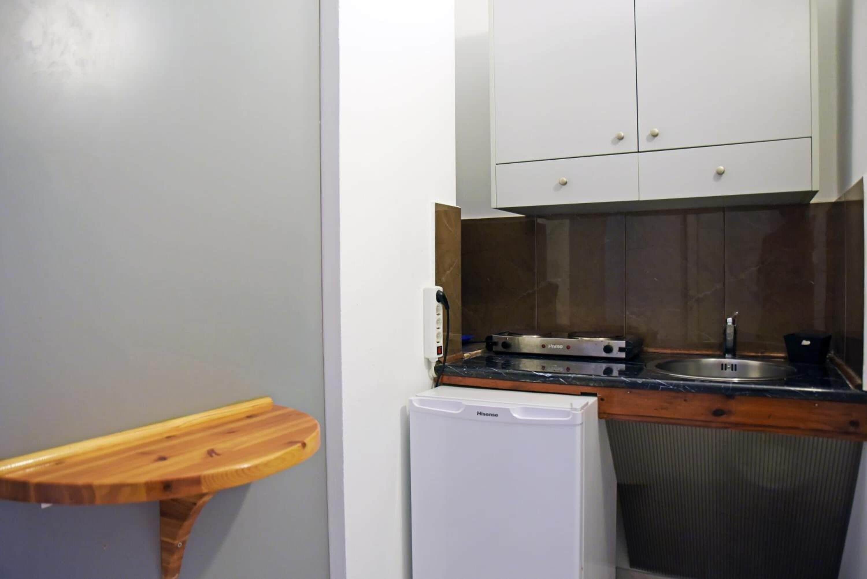 Una cocina compacta con armarios blancos, horno empotrado y un refrigerador pequeño.