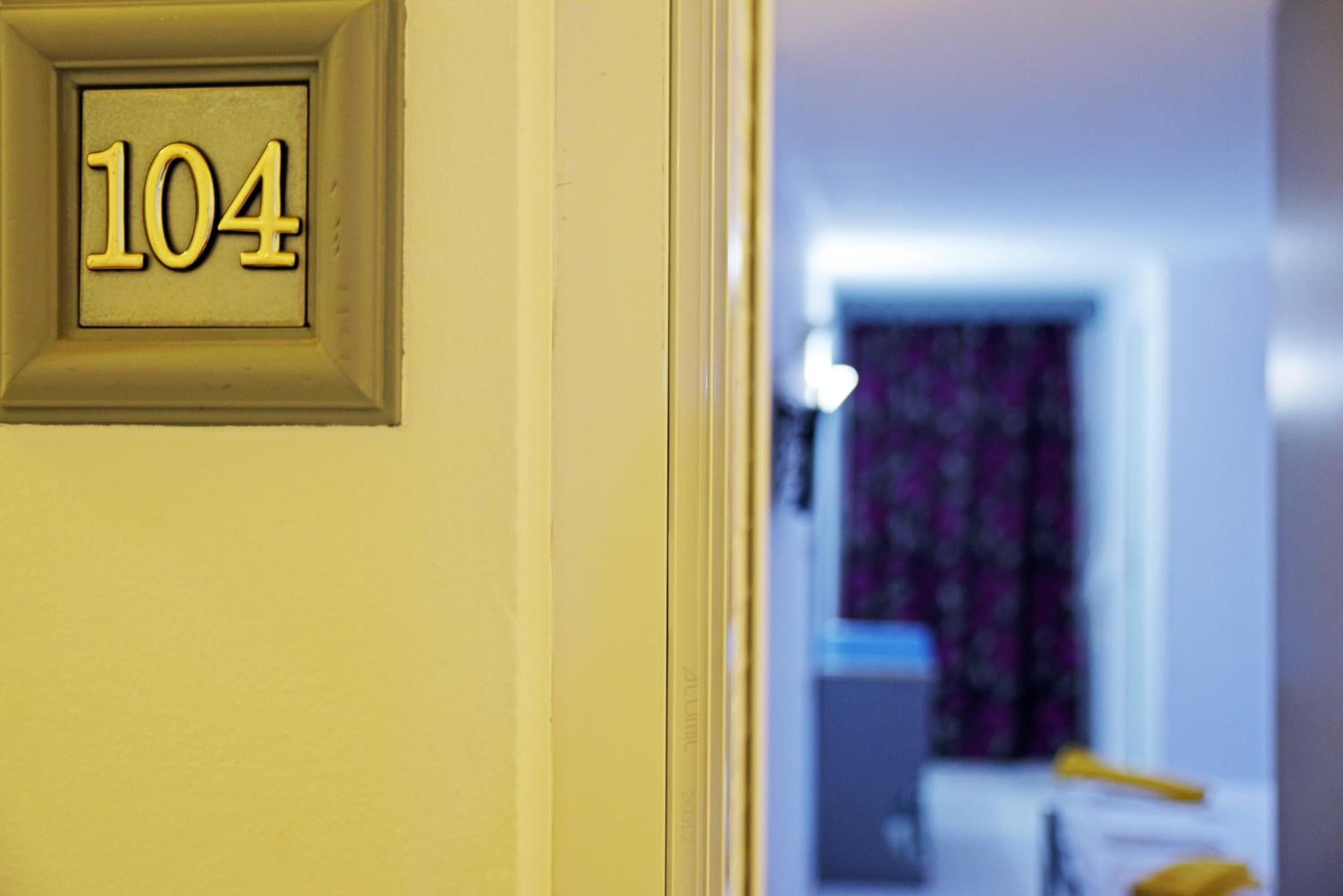 Puerta con el número 104 que da a una habitación con una cama y una mesita de noche.