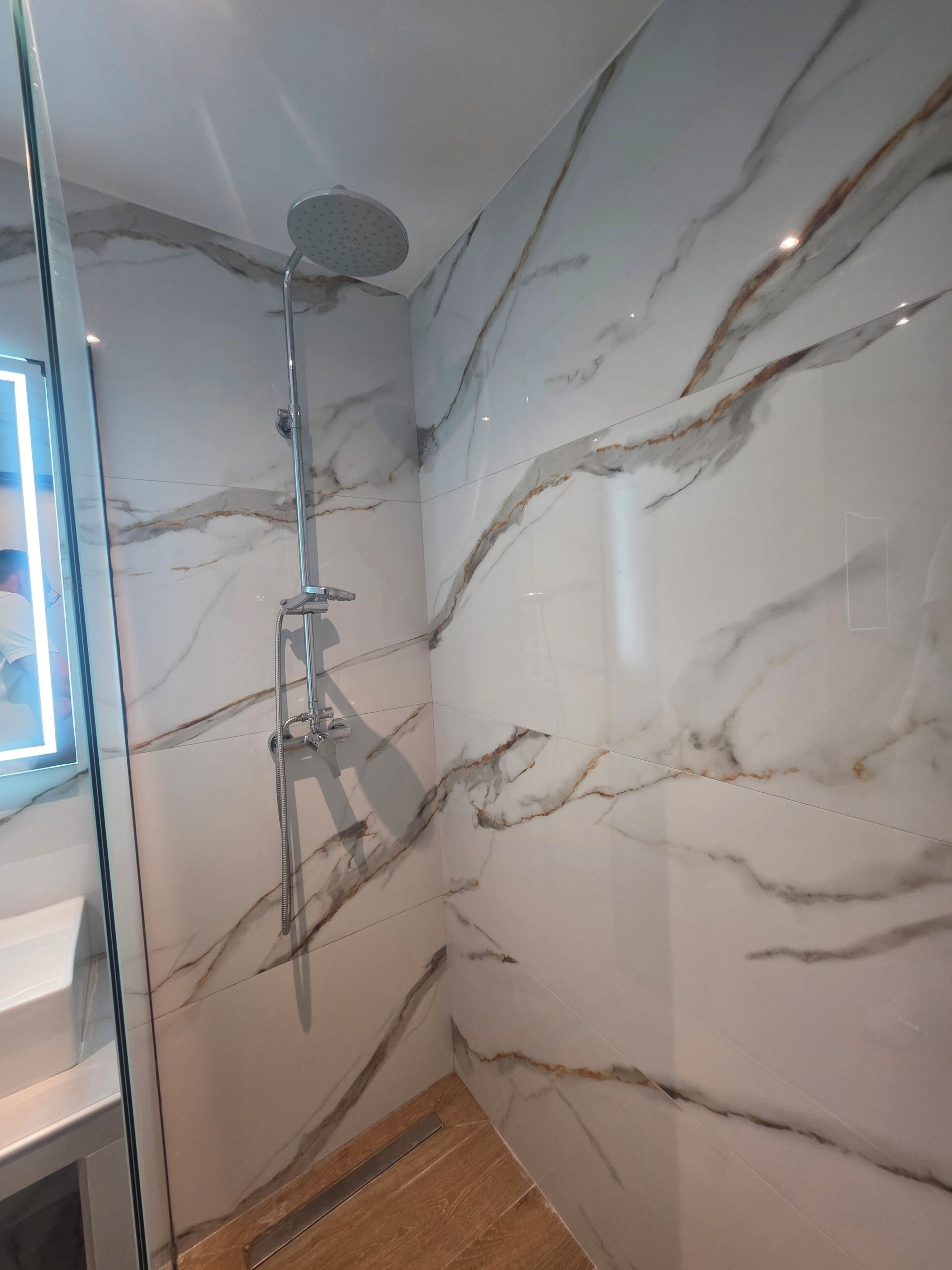 A bathroom with a marble wall, a shower, and a glass door.