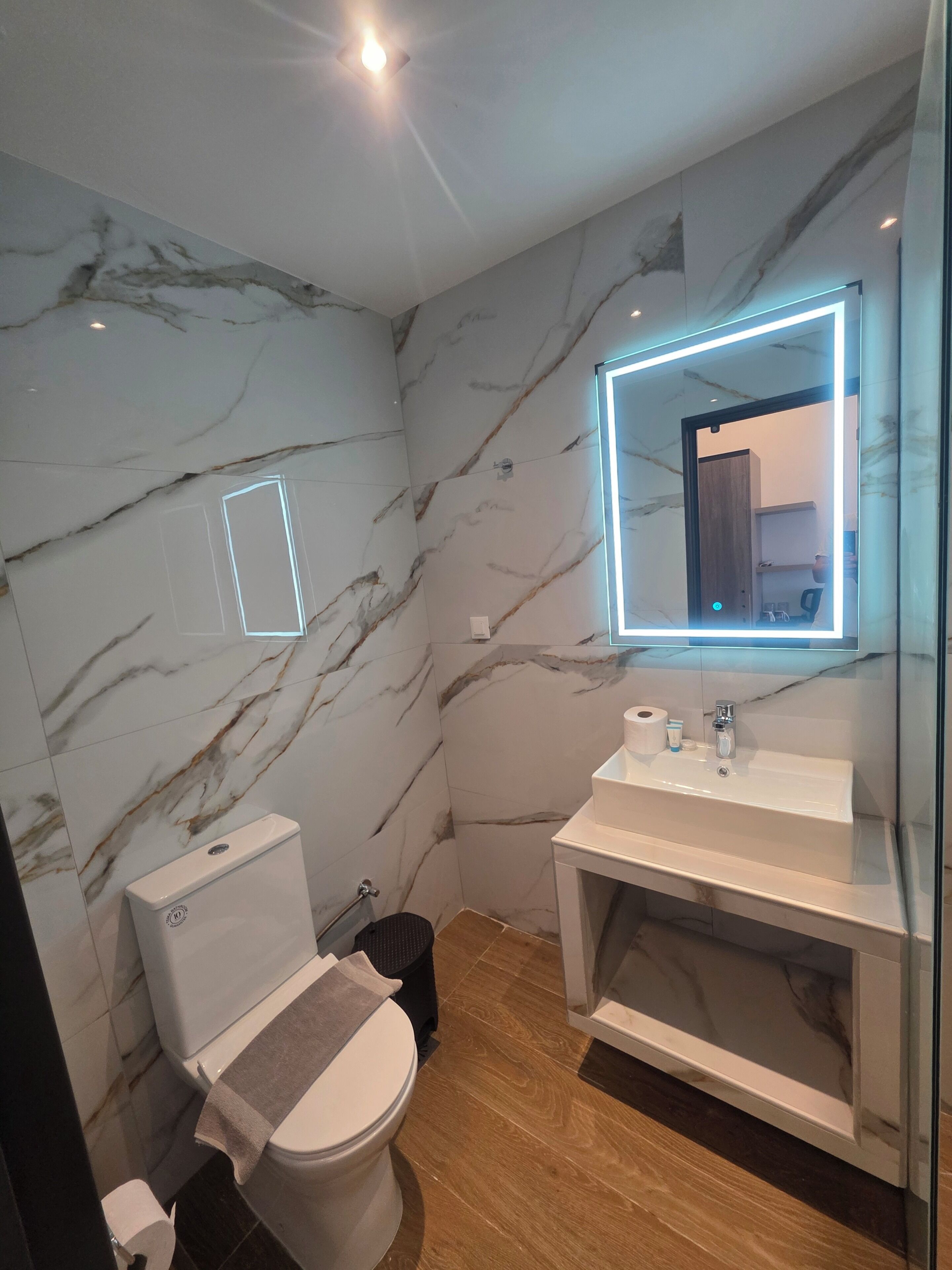 Un baño moderno con paredes de mármol, inodoro, lavabo con espejo y zona de ducha.