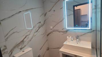 Un baño moderno con paredes de mármol, inodoro, lavabo con espejo y zona de ducha.