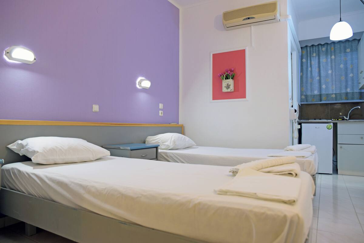 Una habitación de hotel con dos camas, un escritorio pequeño, una ventana con cortinas y un rincón americano.