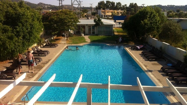 A rectangular swimming pool with a clear blue water, surrounded by lounge chairs and a small building in the background. - Falirala Central (Rhodes)