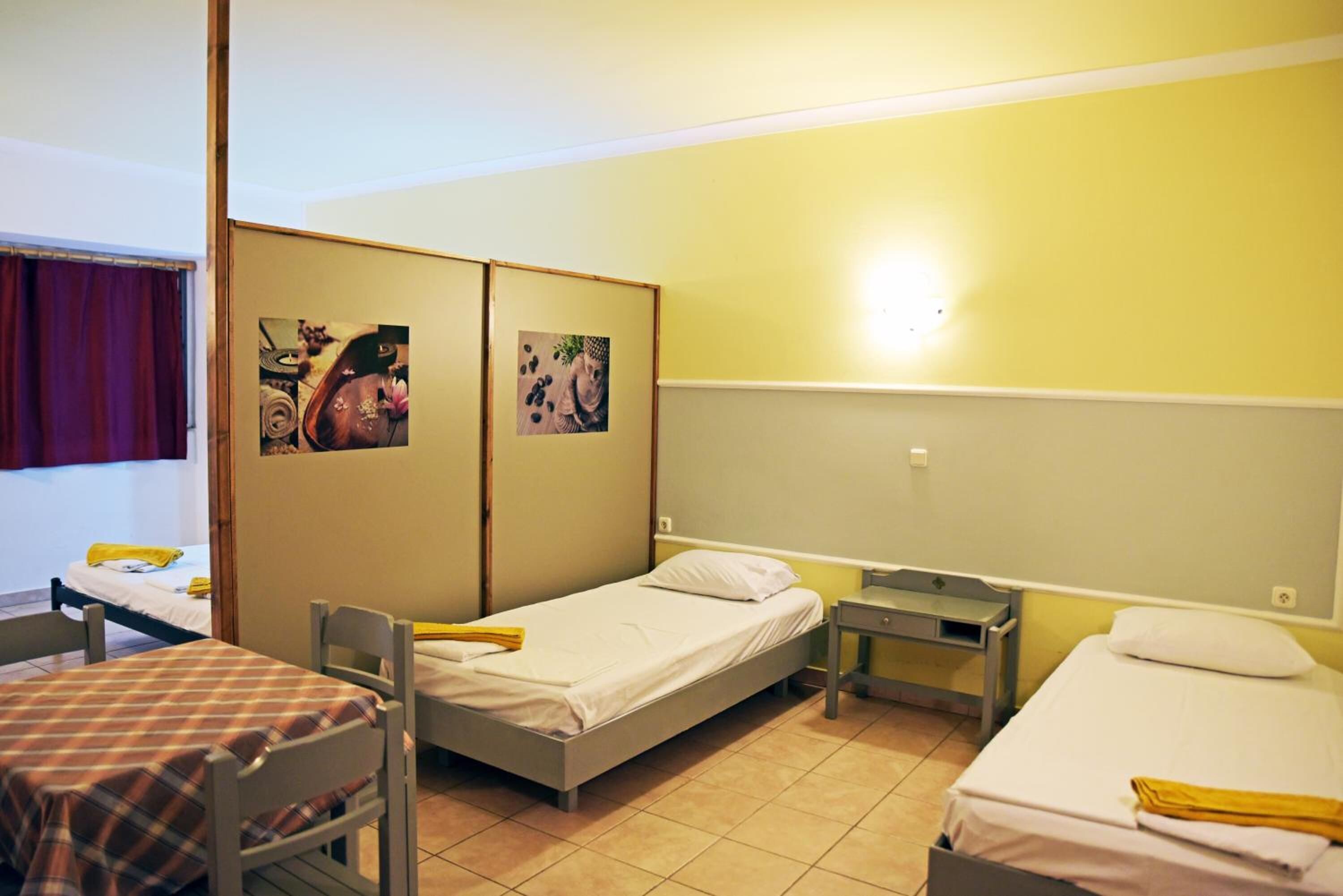 Une chambre avec deux lits simples, une petite table, une chaise et deux armoires fixées au mur.