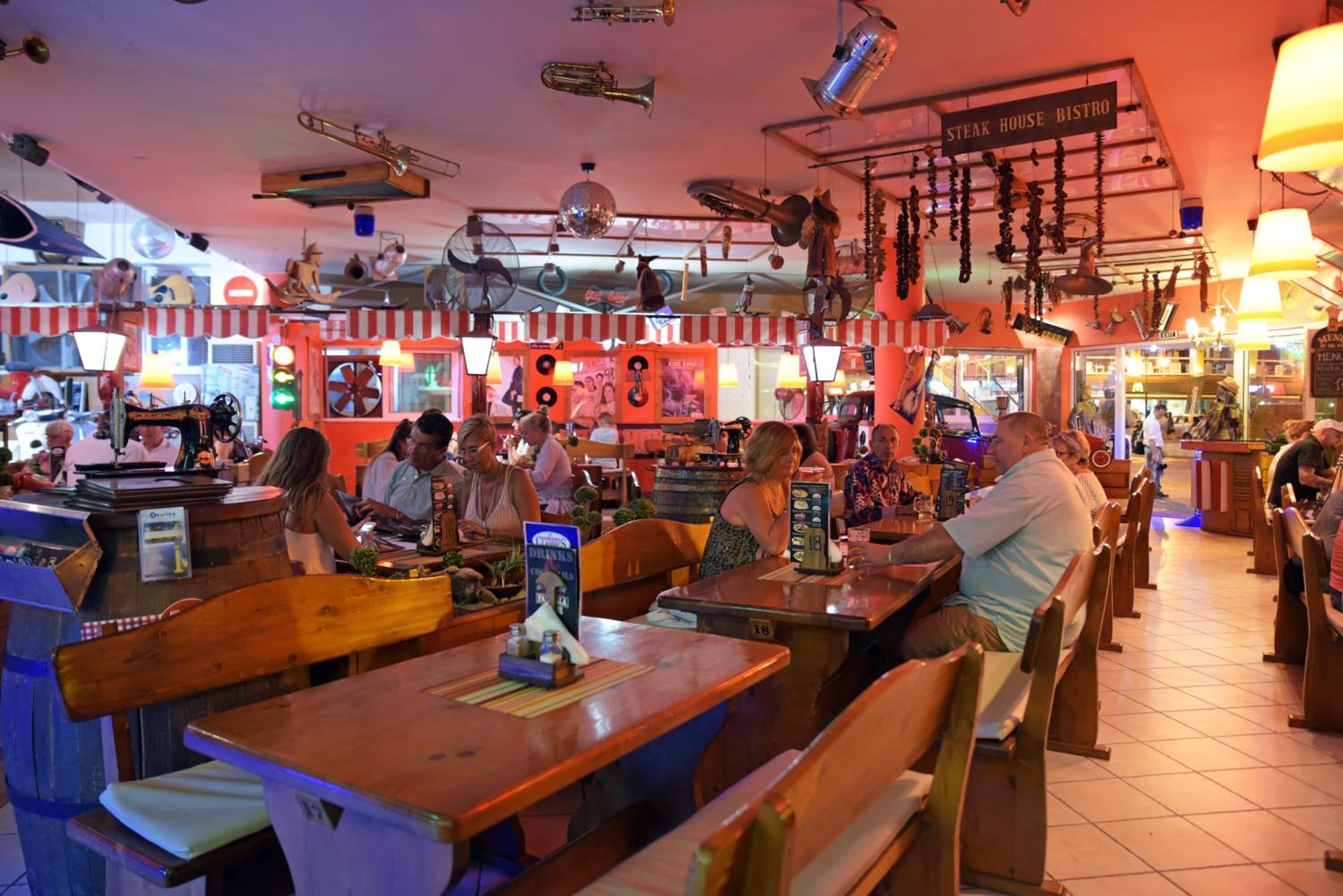 A restaurant interior with wooden tables and benches, a bar area, and various hanging decorations.