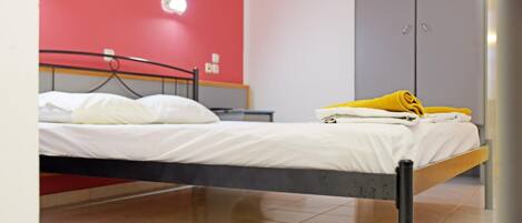 A single bed with white bedding, a yellow towel, and a red wall in the background.
