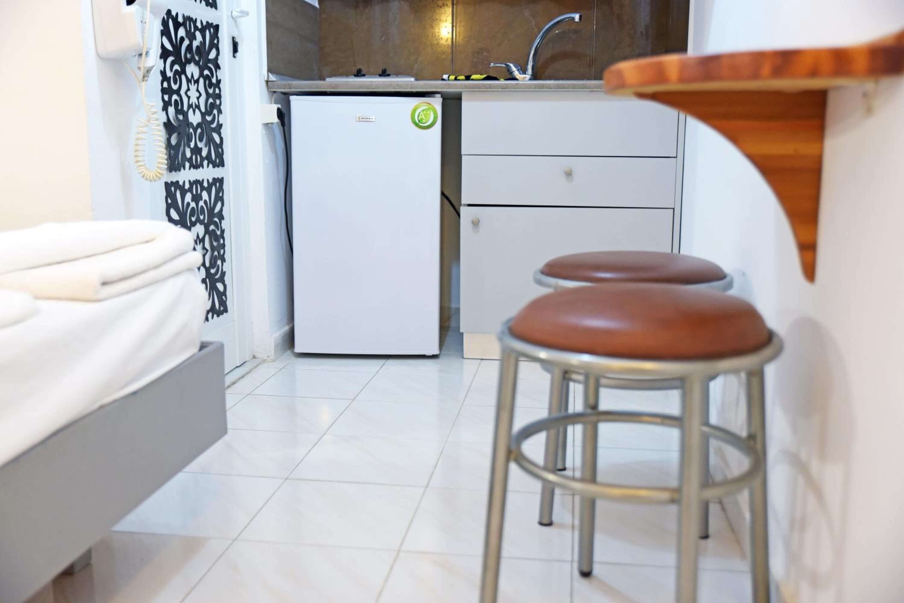 A compact kitchen with a refrigerator, a sink, and a small dining area with stools.