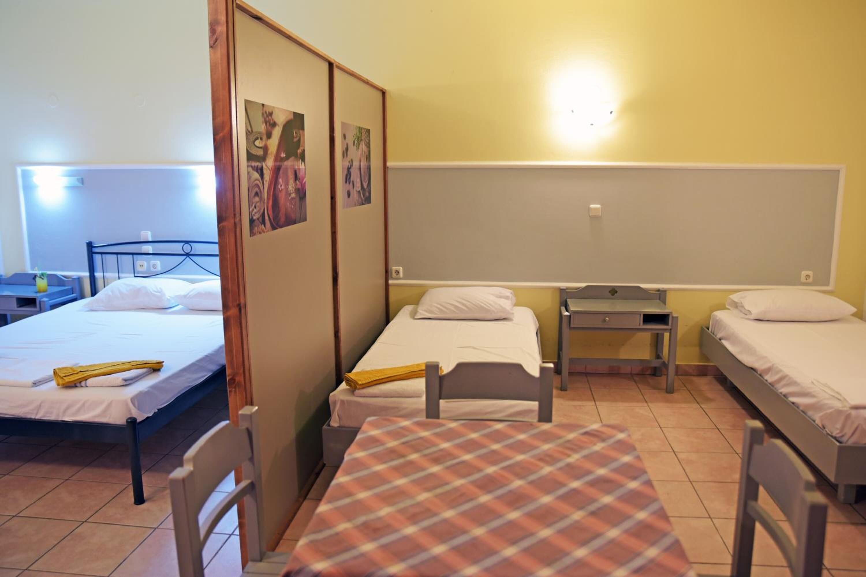 Quarto em dormitório com duas camas de solteiro, uma mesa pequena e uma cadeira.