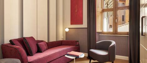 Una habitación moderna con un sofá rojo, un sillón gris, una pequeña mesa blanca y un amplio ventanal con cortinas.