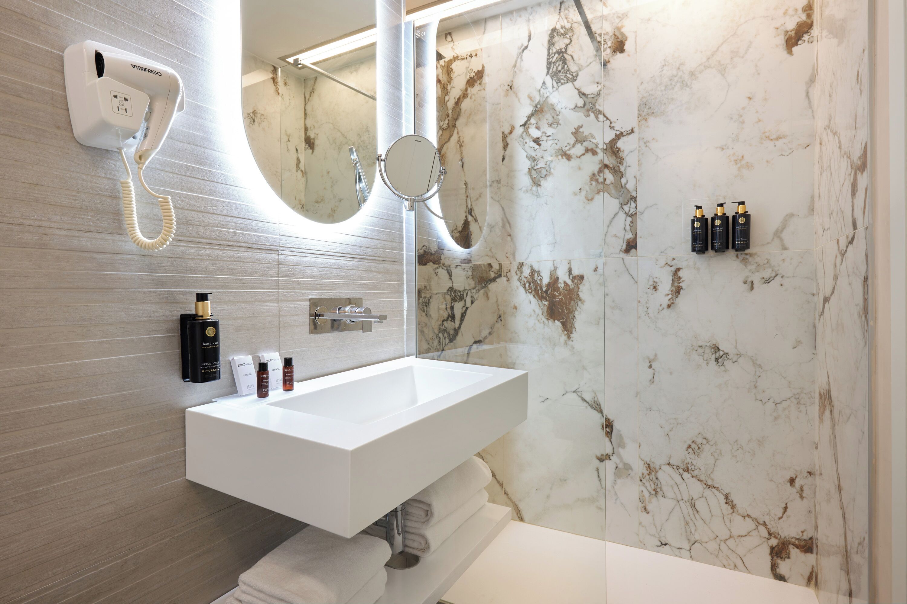 A bathroom with a white sink, a hairdryer, a mirror, and toiletries.