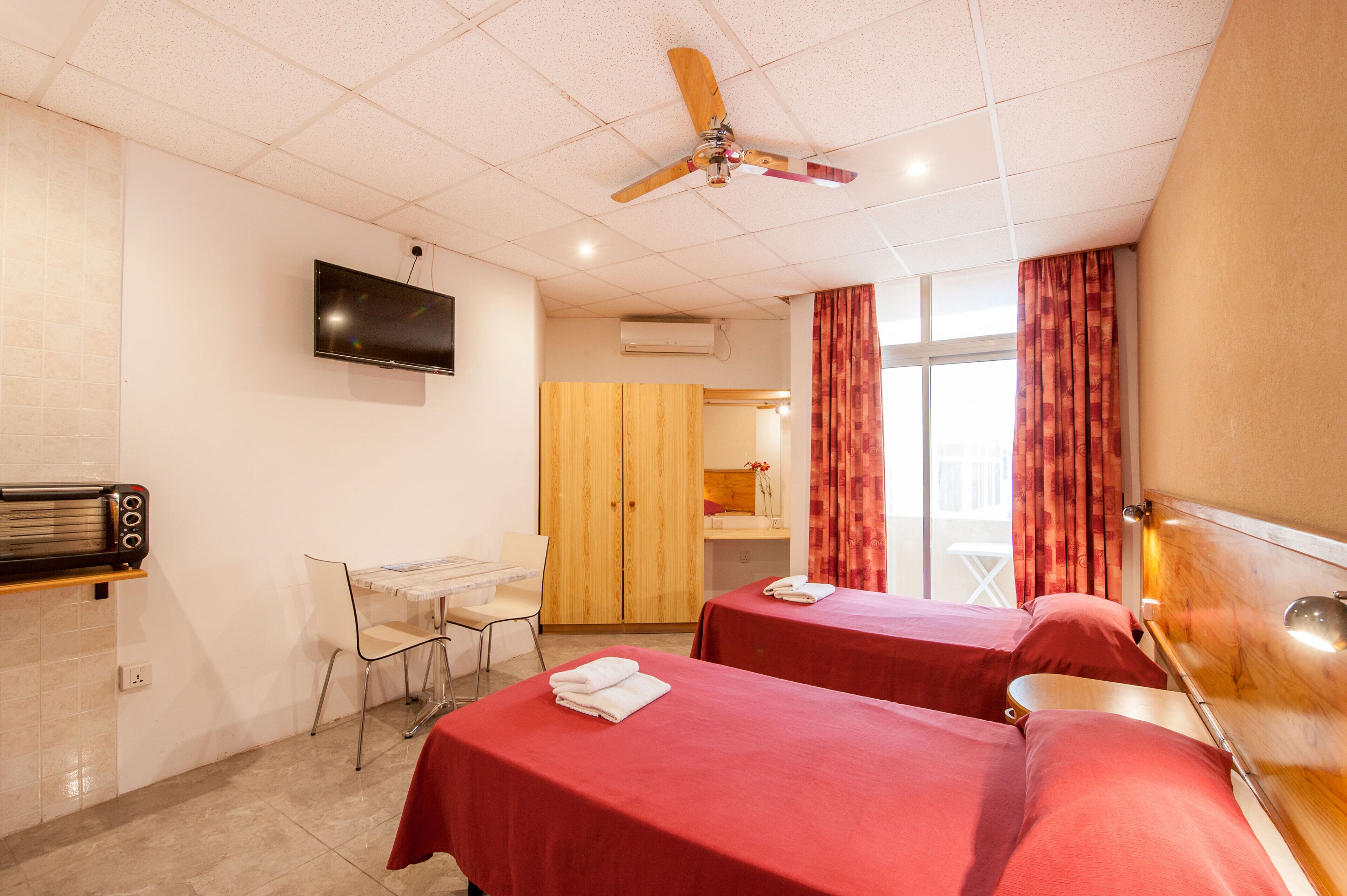 Ein Hotelzimmer mit zwei Betten, einem Schreibtisch, einem Fernseher und einem Deckenventilator.