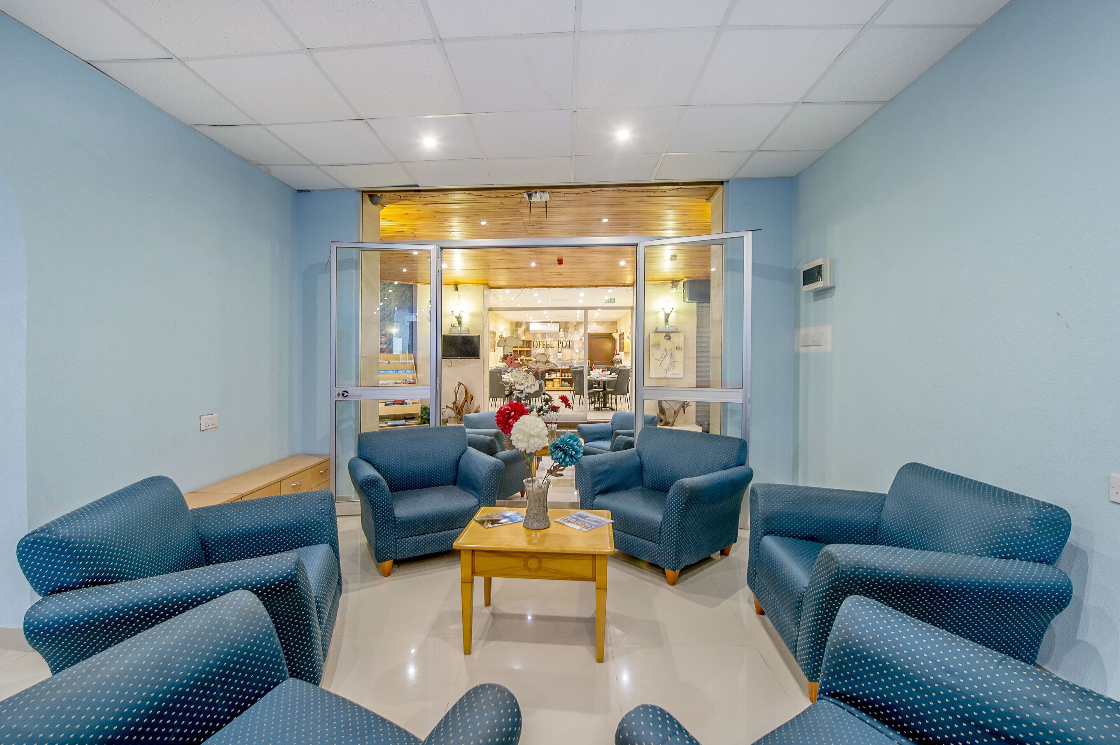 A lobby with blue upholstered sofas, a wooden coffee table, and a view into a dining area.