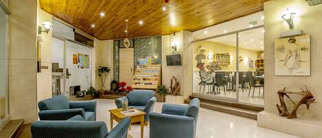 A spacious lobby with a wooden ceiling, comfortable seating, a coffee shop, and a large window with a view of the interior.