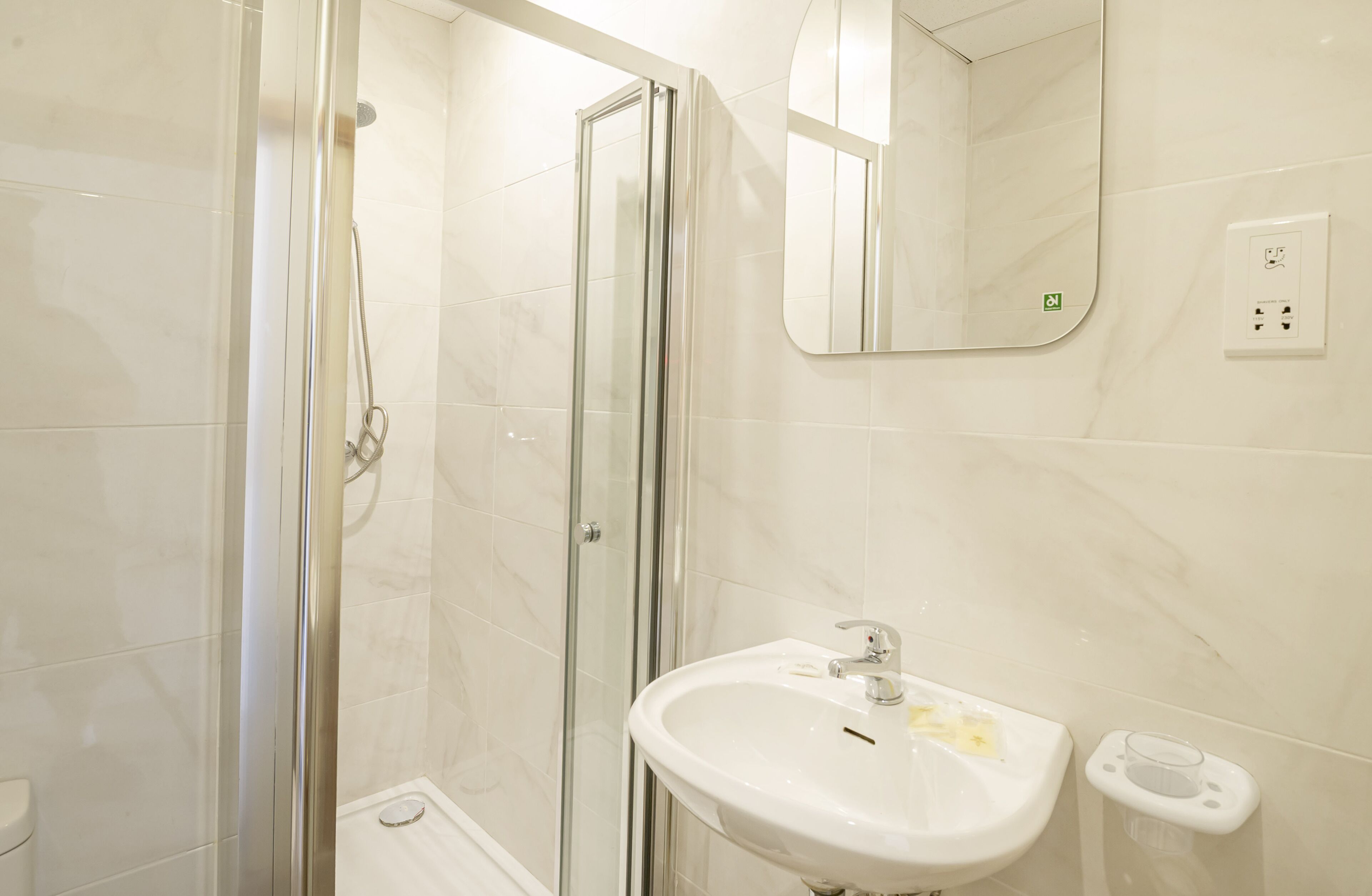 Une salle de bain moderne avec une douche à parois de verre, un lavabo blanc doté d’un porte-savon et un miroir au-dessus du lavabo.