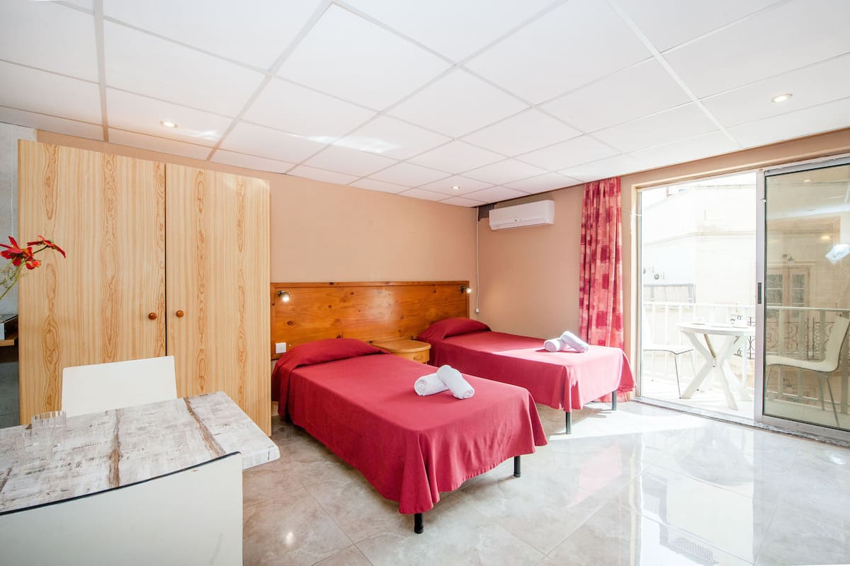 A hotel room with two beds, a wooden wardrobe, a small table, and a glass door leading to an outdoor area.