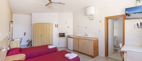 Une chambre d’hôtel avec deux lits, une kitchenette, un ventilateur de plafond, un extincteur et une salle de bain.