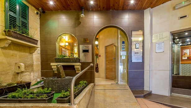 A hotel lobby with a stone wall, a wooden ceiling, and a reception desk. - Alborada Aparthotel (Sliema)