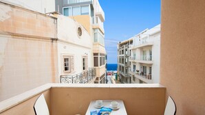 A balcony with a table, two chairs, and a magazine. The balcony overlooks a street with buildings and a view of the sea. - Alborada Aparthotel (Sliema)