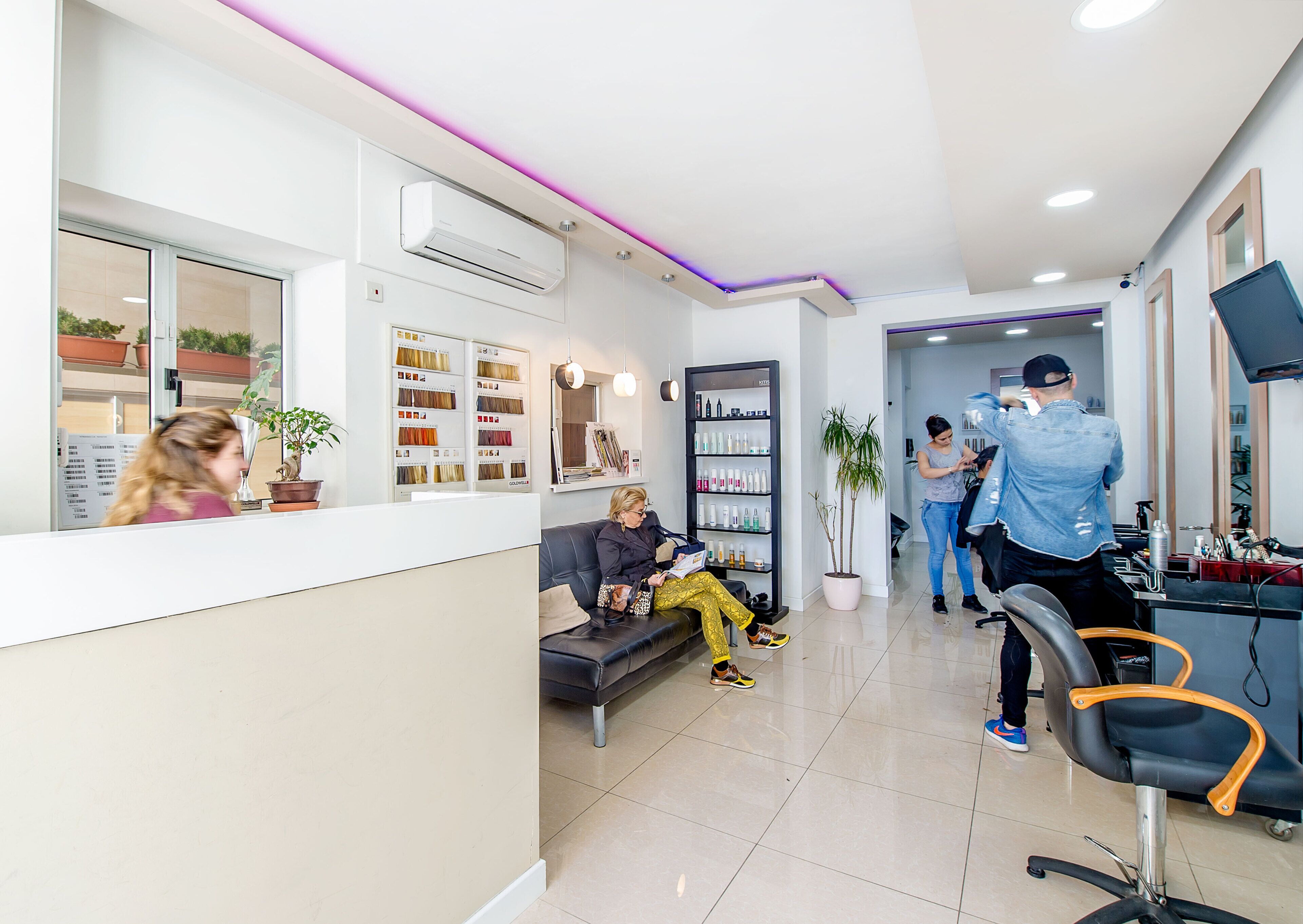 A modern salon interior with a reception desk, seating area, and a hairdressing station.