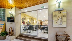 A coffee shop with a modern interior, featuring a large window, wooden ceiling, and a painting on the wall. - Alborada Aparthotel (Sliema)