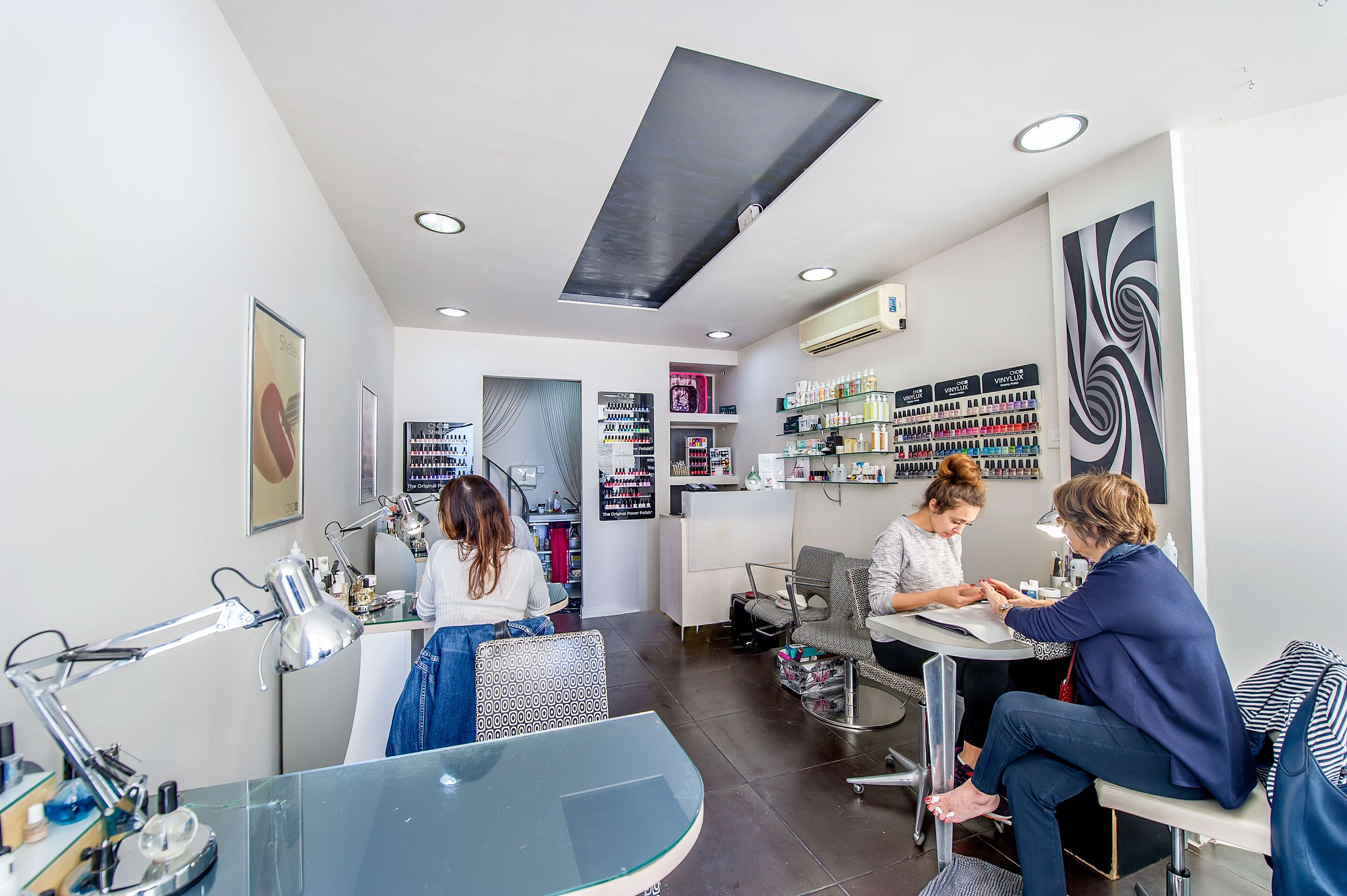 A modern salon interior with a reception desk, seating area, and various beauty products on shelves.