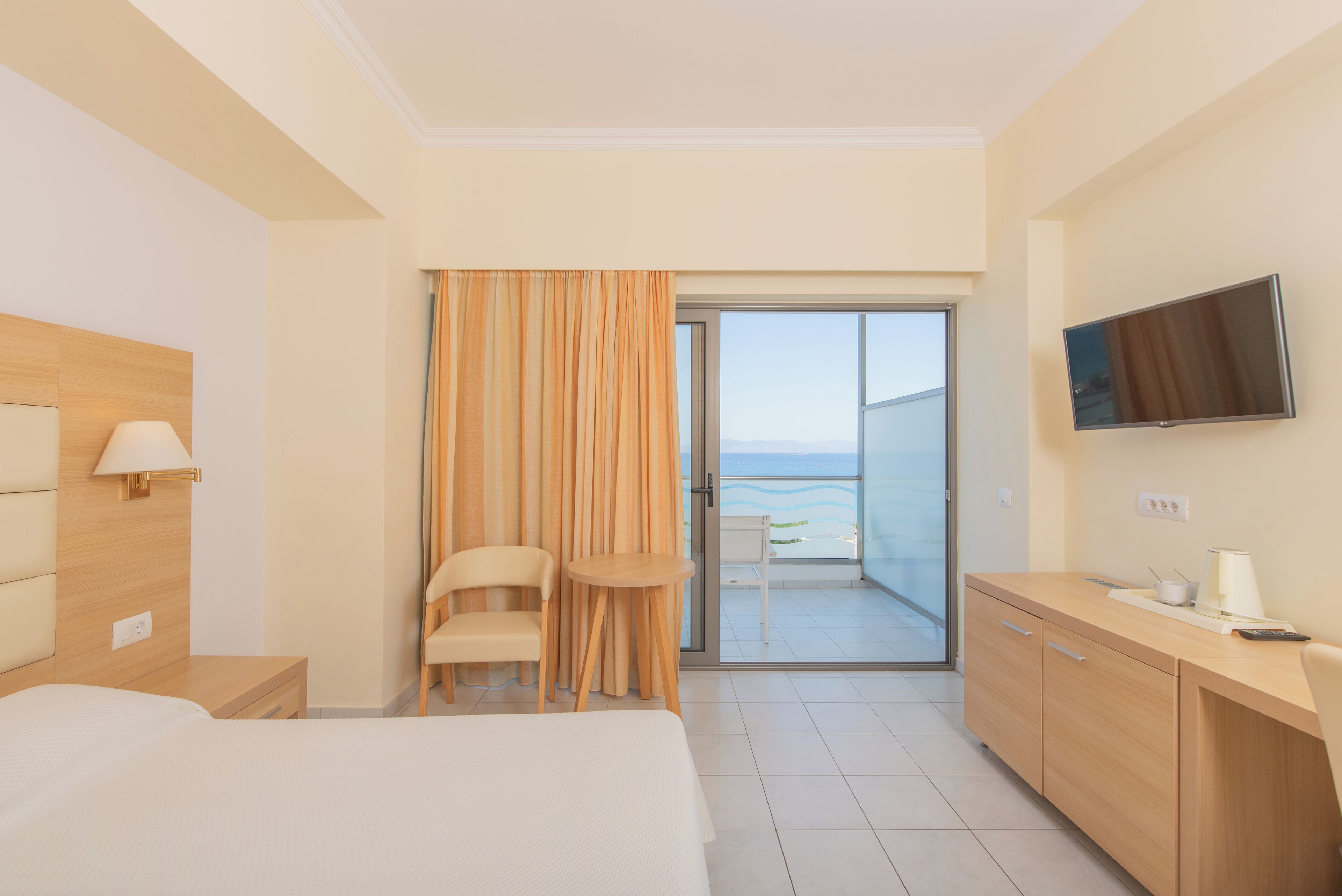 Habitación de hotel con cama, escritorio, silla, televisor y balcón con vista al mar.