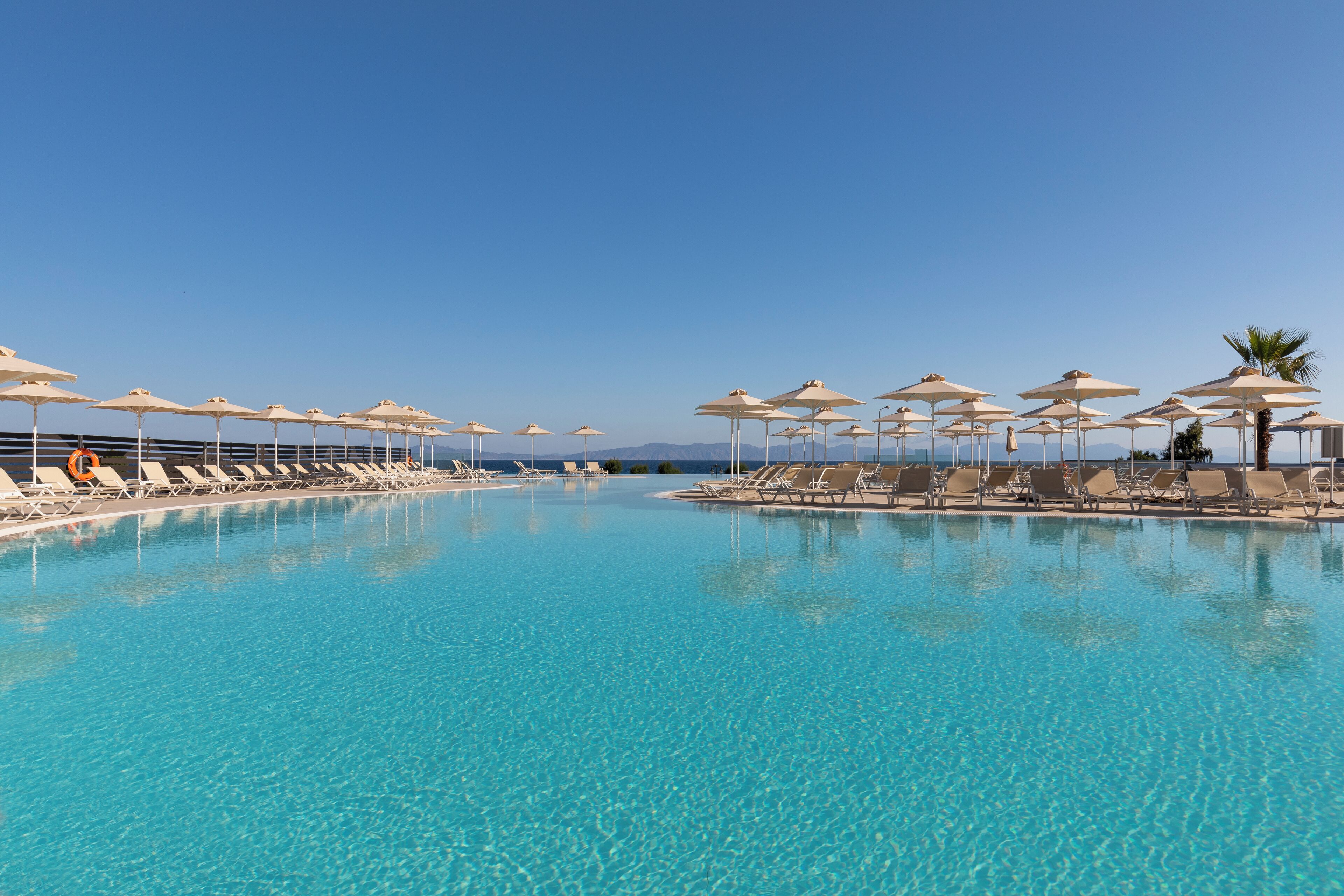 A clear blue pool with sun loungers and umbrellas, surrounded by a clear sky.