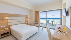 Une chambre d’hôtel avec un lit, une table de chevet, une lampe, une chaise, une table pour le petit-déjeuner et une vue sur la plage.