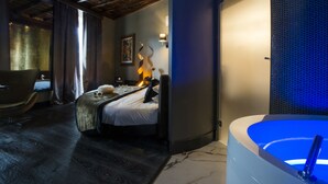Una moderna camera d'albergo con un letto, un'area salotto con una poltrona, una grande vasca da bagno e un soffitto in legno.