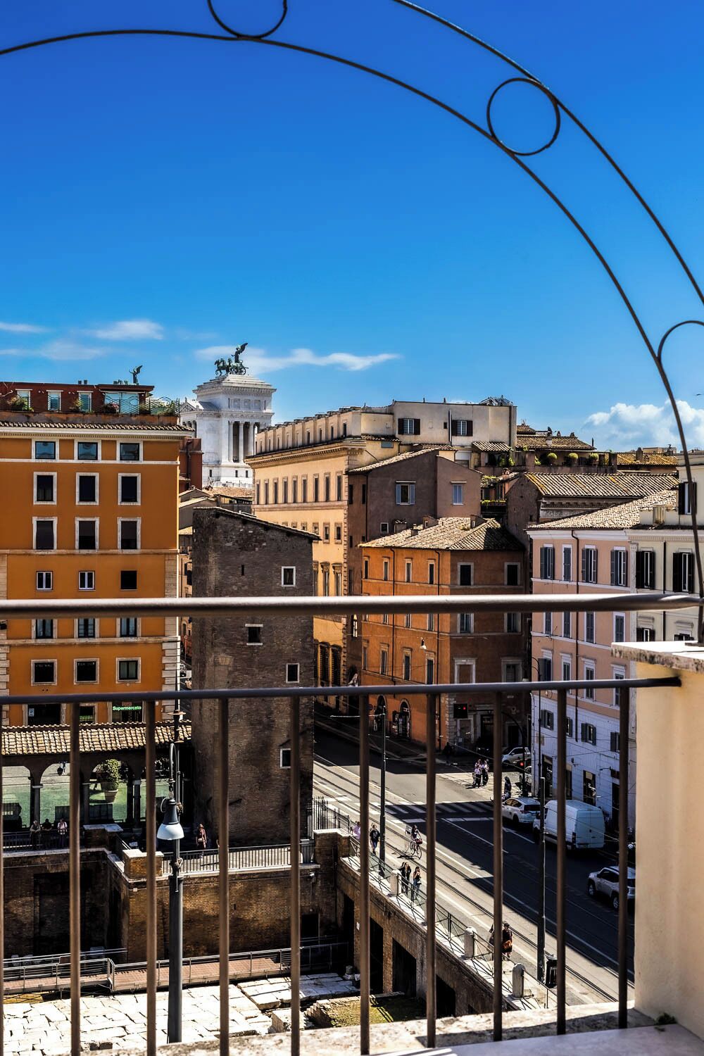A cityscape with historic buildings, a prominent monument, and a clear blue sky.