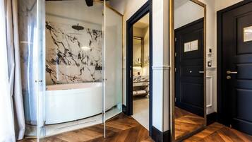 Um banheiro moderno com parede de mármore, box de vidro e piso de madeira.
