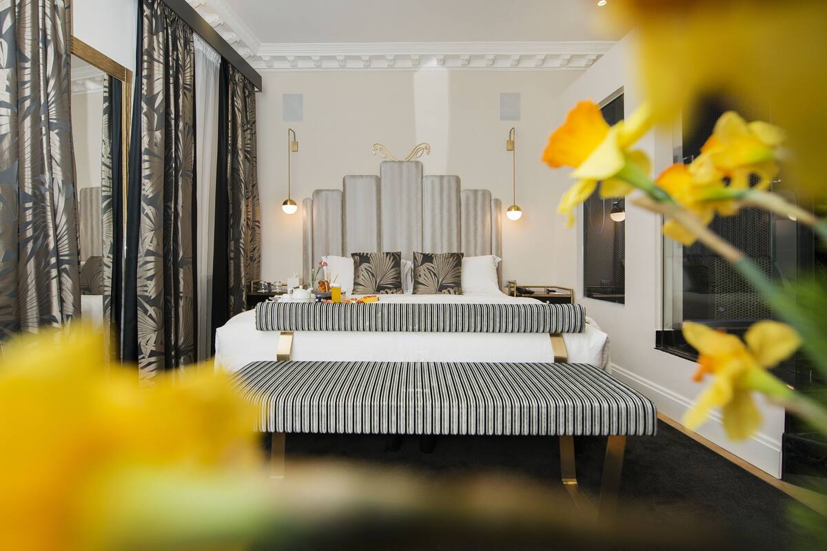 A bedroom with a bed, bedside tables, a bench, and a large mirror.