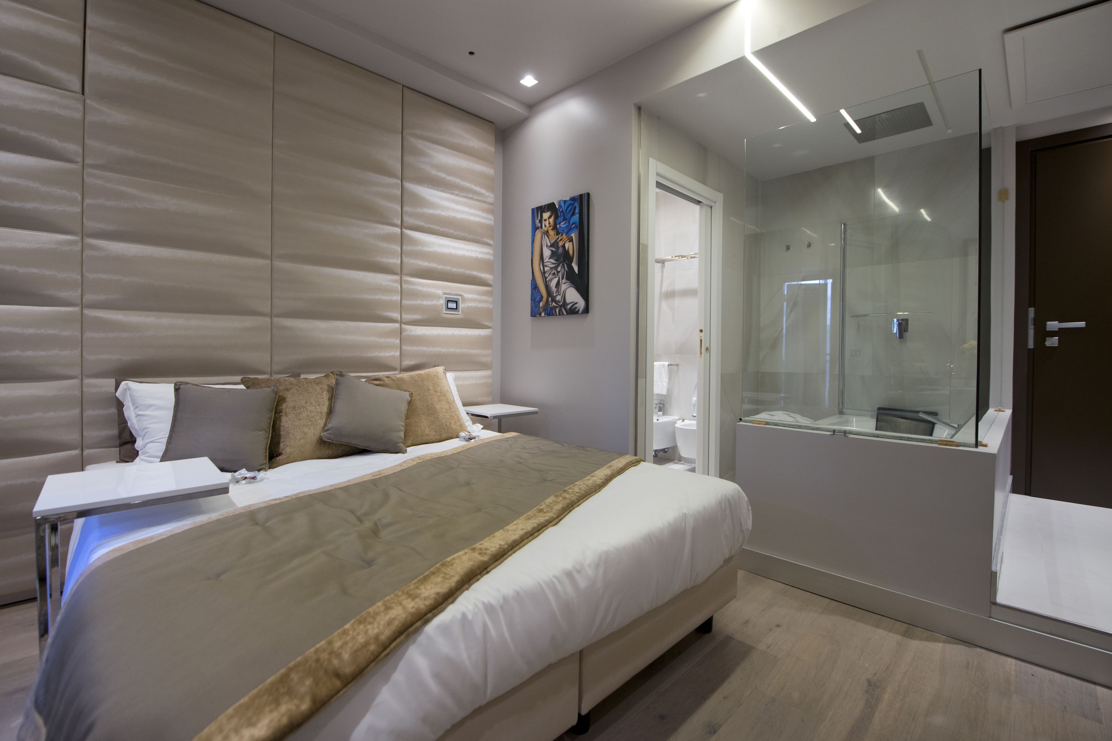 Una habitación de hotel moderna con una cama grande, una mesita de noche, un box de ducha de vidrio y un cuadro en la pared.