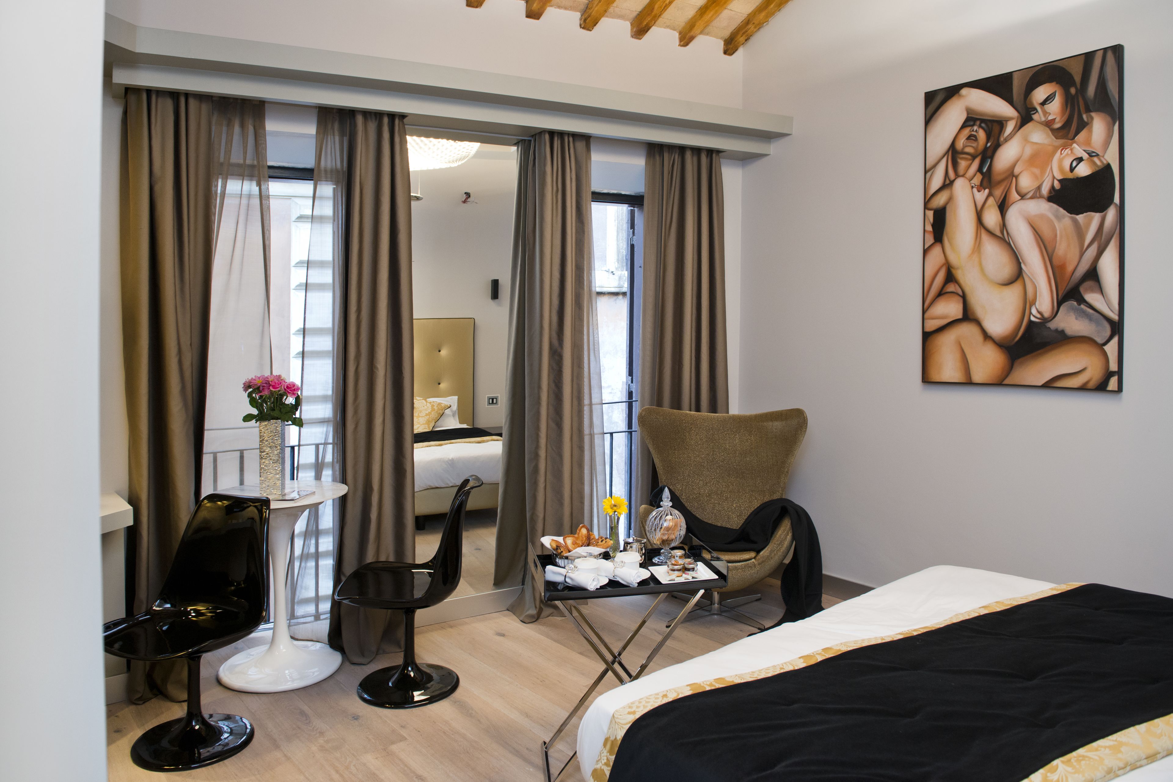 A hotel room with a bed, a chair, a small table with a vase of flowers, and a painting on the wall.