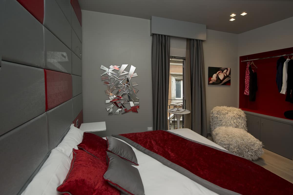 A modern bedroom with a large bed, a fluffy chair, and a red accent wall.