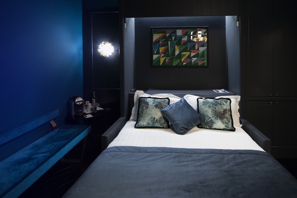 Une chambre à coucher avec un lit, des oreillers, une table de chevet, une lampe et une œuvre d’art murale.